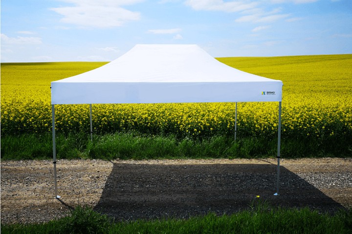 Witte tent bij koolzaad: Een witte, opvouwbare klaptent (schaarconstructie) geplaatst aan de rand van een koolzaadveld, die een frisse en professionele ruimte biedt voor zomerse promotieacties in de n