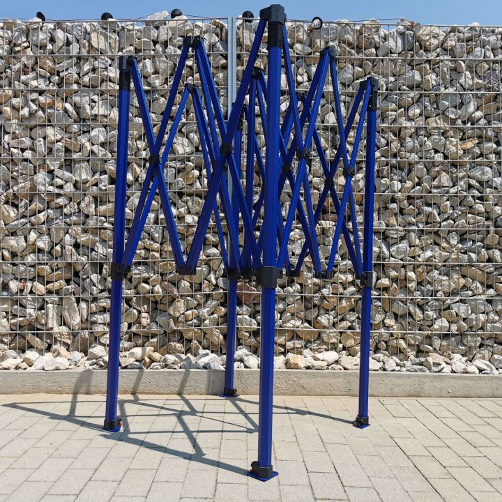 Uitgevouwen, maar niet geschoten blauwe constructie (frame) van een partytent met schaarmechanisme, staande op een betegelde vloer met steentjes op de achtergrond (bij de omheining).