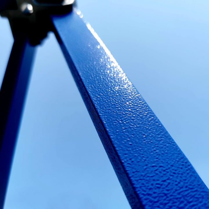 Detail van de blauwe metalen staaf/poot van de tent met een fijn gestructureerd oppervlak (waarschijnlijk poedercoating) tegen de blauwe lucht.