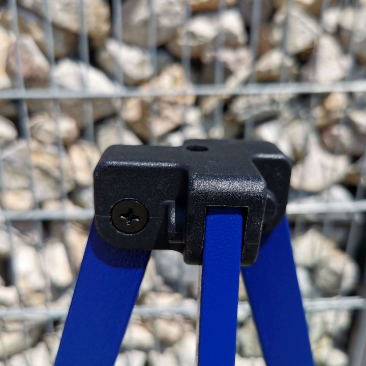 Detail van het zwarte plastic verbindingsstuk (bovenste deel van het been) op de blauwe constructie van de tent, met een achtergrond van grijze steentjes/grind.